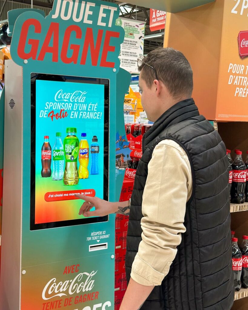 Borne de jeu interactive Coca-Cola en magasin pour renforcer le branding, animer le point de vente et créer une expérience retail engageante.